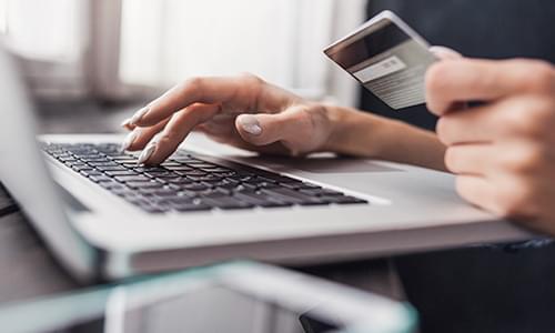 Close-up of hands typing on a laptop with a credit card for updating donor records