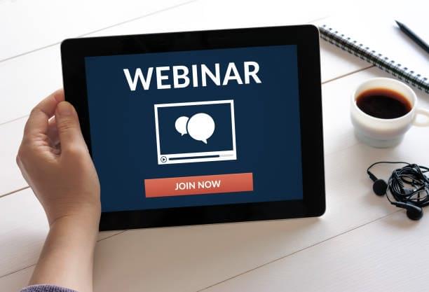 Tablet displaying a 'WEBINAR' sign-up button with coffee and pen